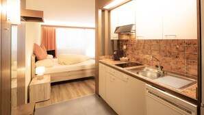 A compact kitchen with a built-in stove, sink, and dishwasher. A bed with pillows is adjacent to the kitchen, and a window provides natural light. - Casa Viva (Bad Ragaz)
