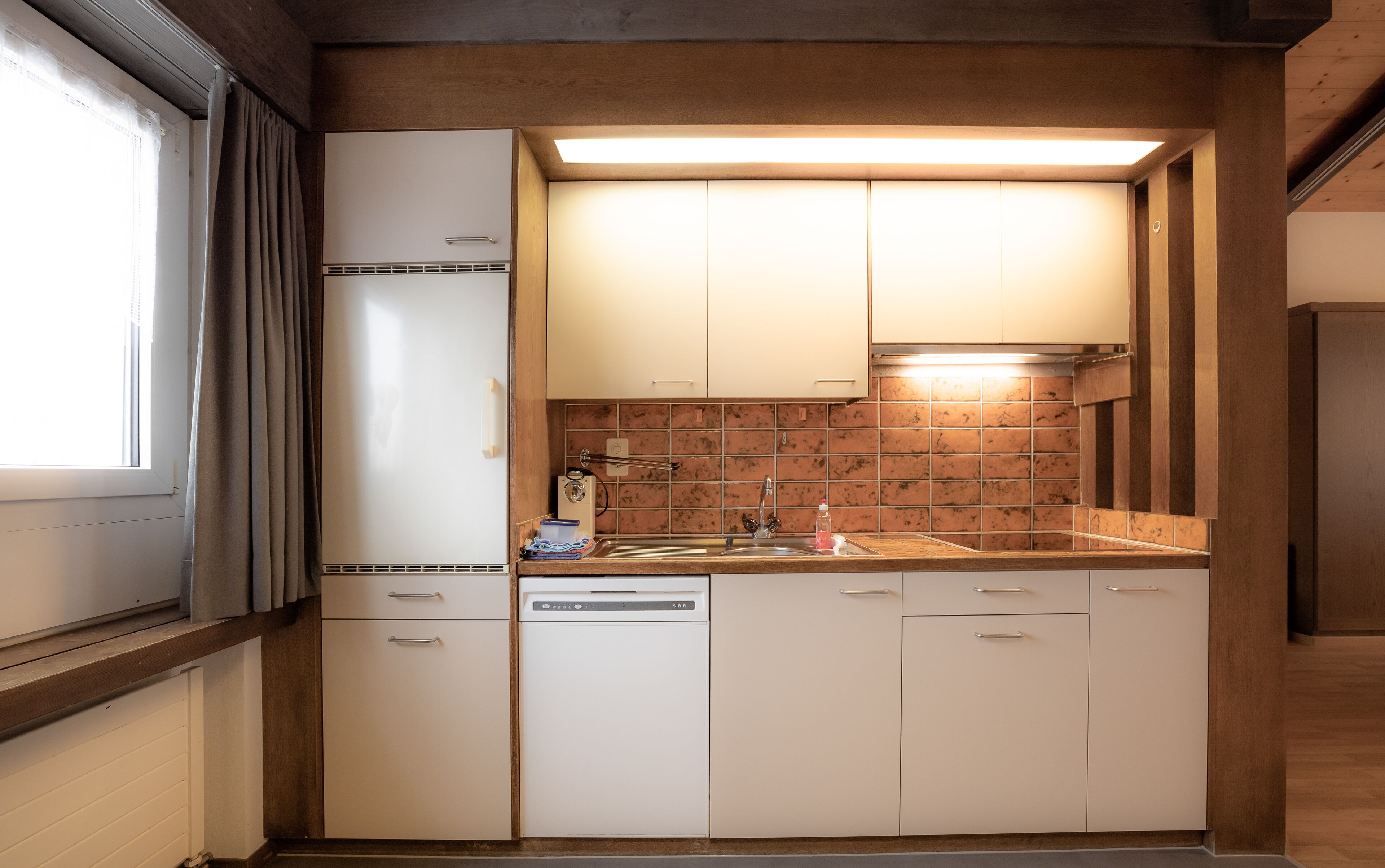 A compact kitchen with white cabinets, a built-in dishwasher, and a tiled backsplash.