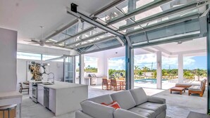 A spacious living area with a large glass door leading to a pool, a kitchen with modern appliances, and a comfortable seating area. - Vacation Villa Oceanview Hotel Amenities (Providenciales)