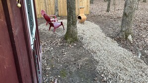 A wooden deck with Adirondack chairs, a bird feeder, and a gravel path.