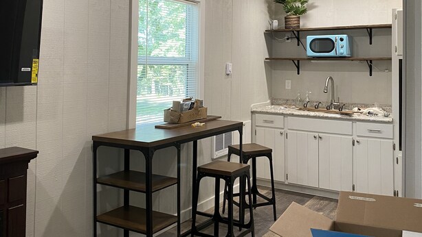 A kitchen with wooden ceiling, white cabinets, a microwave, and a sink.