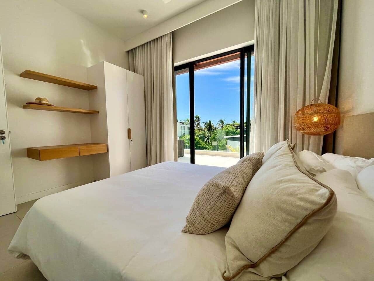 Une chambre d’hôtel moderne, dotée d’un grand lit, d’étagères intégrées et offrant une vue sur les palmiers.