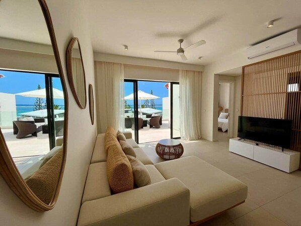 A modern living room with a sofa, TV, and large windows overlooking a pool area.