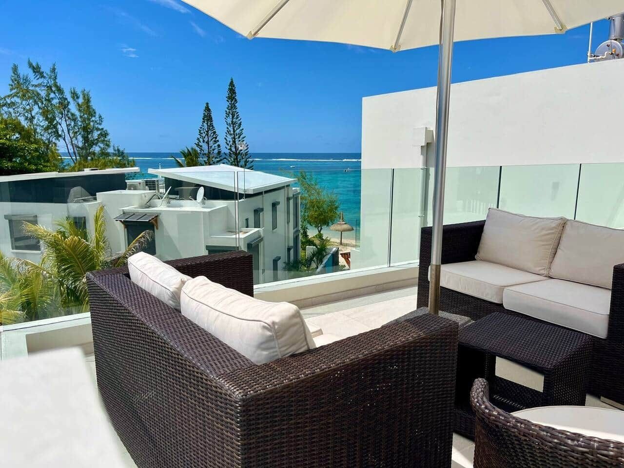 A balcony with wicker furniture, a glass railing, and a view of the ocean.