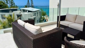 A balcony with wicker furniture, a glass railing, and a view of the ocean. - Exclusive beachfront penthouse (Belle Mare)