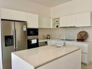 Una cocina moderna con refrigerador de acero inoxidable, horno integrado y una isla grande con pileta.