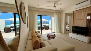 A modern living room with a sofa, TV, and large windows overlooking a pool area. - Exclusive beachfront penthouse (Belle Mare)