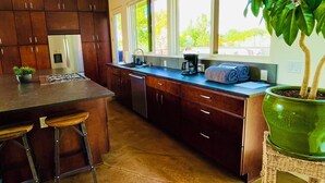 Een moderne keuken met donkerhouten kastjes, een centraal eiland met barkrukken, een groot raam en een potplant.