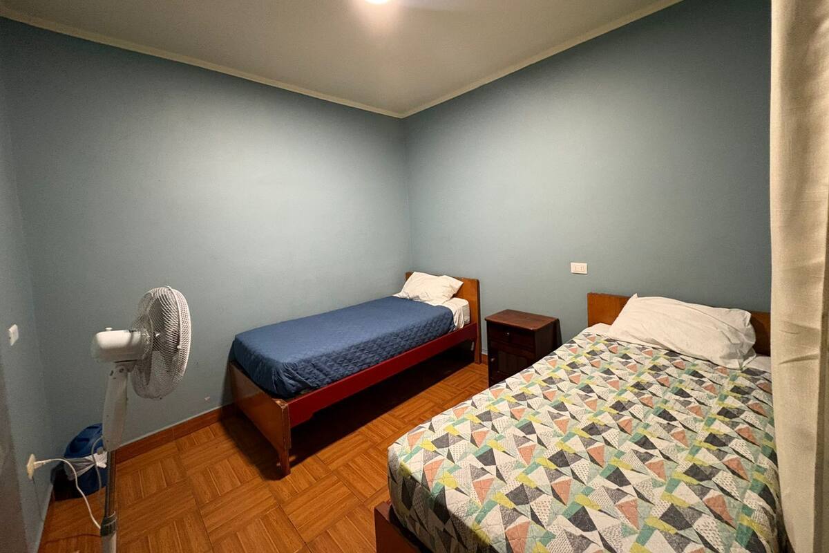 Ein Schlafzimmer mit zwei Betten, einem Standventilator und einem kleinen Nachttisch.
