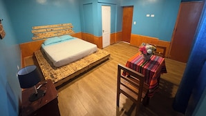 A bedroom with a bed, bedside table, lamp, chair, and a small table with a floral arrangement. - Raymi House Hostel (Arica)