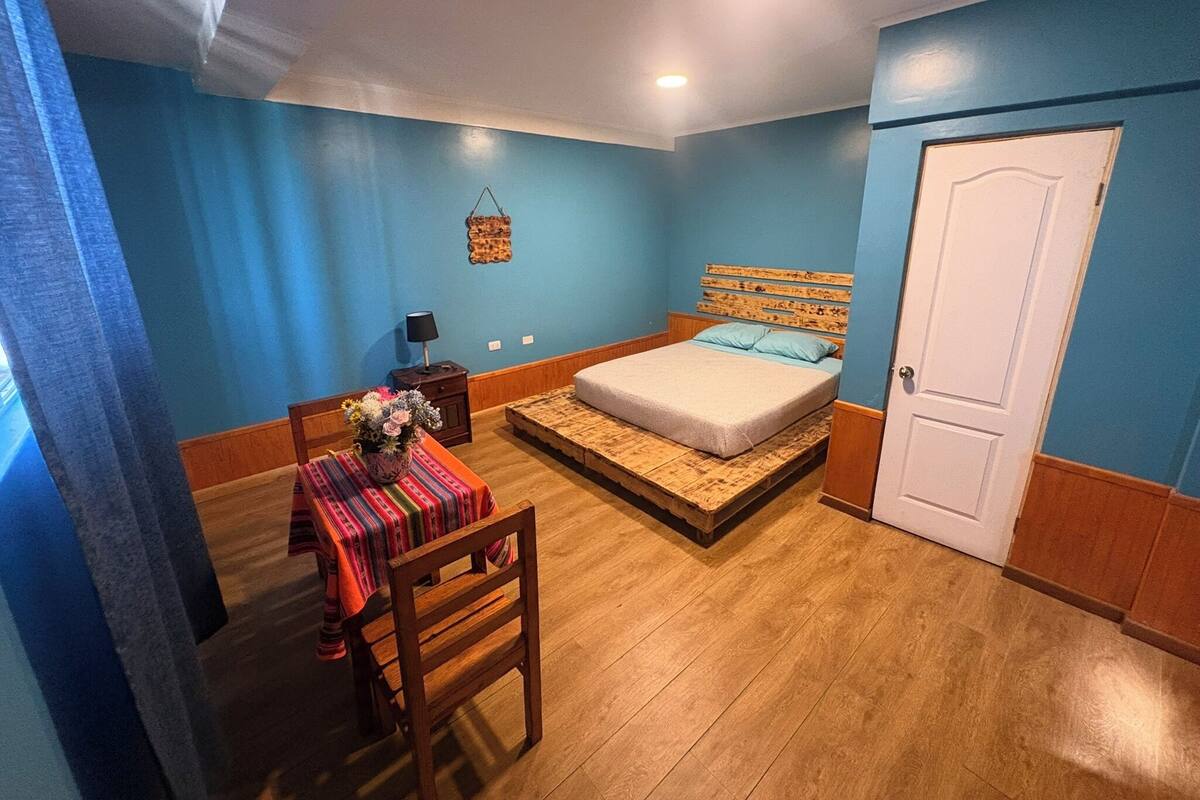 Ein Schlafzimmer mit Bett, Nachttisch, Stuhl, Tisch mit Tischdecke und einer Tür.