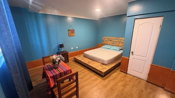 Un dormitorio con una cama, una mesita de noche, una silla, una mesa con mantel y una puerta.