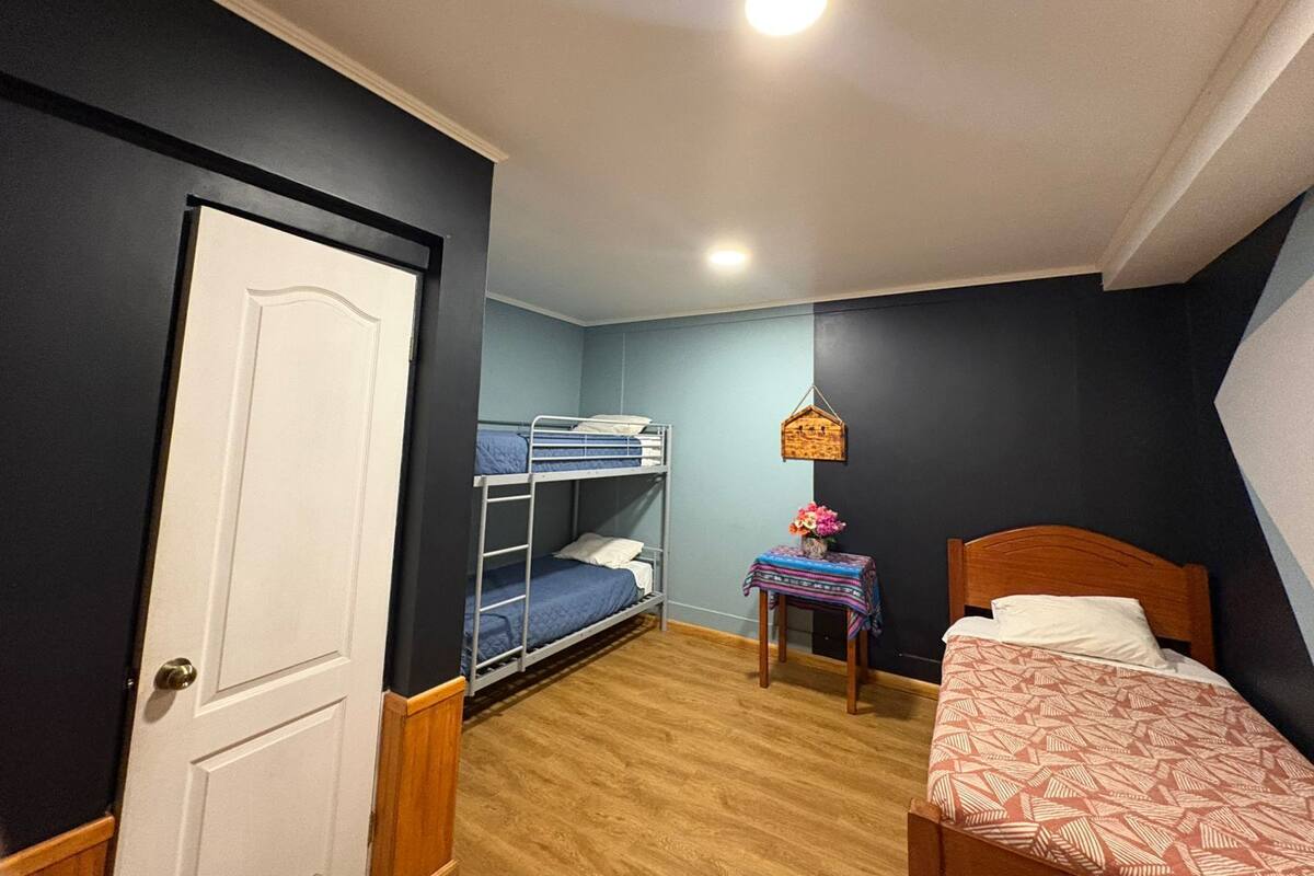 Ein Zimmer mit einem Etagenbett, einem Einzelbett, einem kleinen Tisch mit einer Vase und einer Tür.