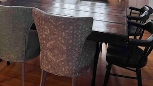 Un coin repas avec une table et des chaises en bois, de grandes fenêtres avec des rideaux et un lustre.