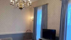 Un salon avec un canapé gris, une petite table basse, un téléviseur posé sur un meuble gris, un lustre et un tapis à motifs.
