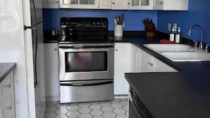 Une cuisine avec des armoires blanches, un plan de travail noir, une cuisinière en acier inoxydable et un réfrigérateur blanc.