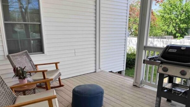 Une véranda couverte avec deux fauteuils en osier, un petit pouf rond et un barbecue.