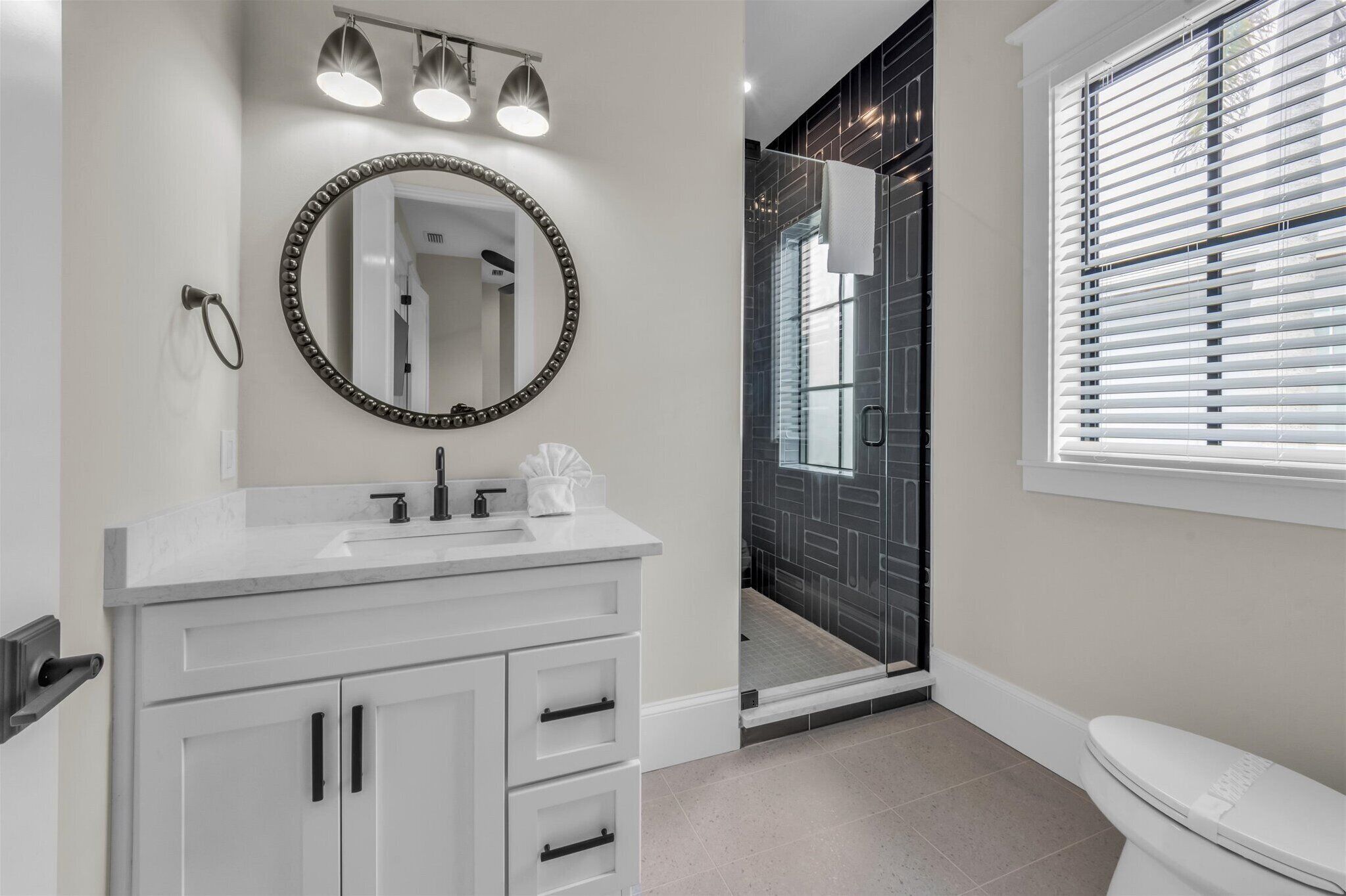 A modern bathroom with a white vanity, a large mirror, and a shower area with black tiles.