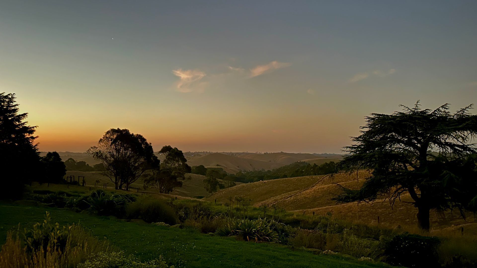 A landscape with rolling hills, trees, and a clear sky.