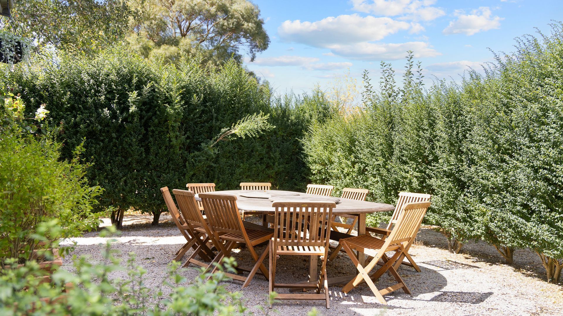 Une table ronde en bois, entourée de six chaises, dans un jardin.