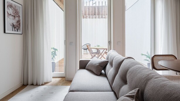 A modern living room with a grey sofa, a dining table with chairs, and a sliding glass door leading to an outdoor area.