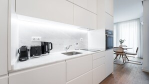 A modern kitchen with white cabinetry, a built-in oven, and a dining area with a table and chairs.