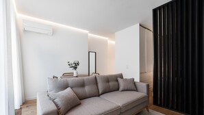 A modern living room with a grey sofa, a small table with a vase, and a black vertical panel.