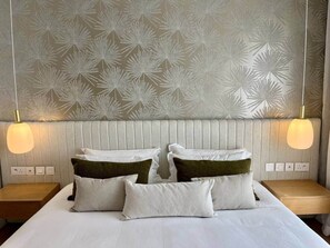 Une chambre d’hôtel comprenant un lit, deux tables de chevet, un mur orné d’un motif de feuilles et deux lampes fixées au mur.