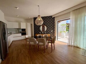 A modern kitchen with white cabinets, a dining area with a glass table, and a large window with curtains.