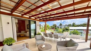 A covered outdoor seating area with wicker furniture, a round coffee table, and a view of the surrounding landscape. - Breathtaking seaview penthouse (Belle Mare)