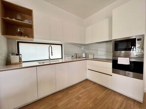 Une cuisine moderne avec des meubles blancs, un four en acier inoxydable et une fenêtre au-dessus de l’évier.