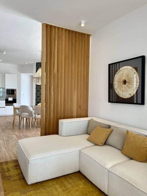 Un salon moderne avec un canapé d’angle, une cloison en bois et une œuvre d’art abstraite accrochée au mur.