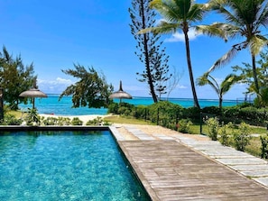 Une piscine aux eaux cristallines, dotée d’une terrasse en bois, entourée d’une végétation tropicale et offrant une vue sur l’océan.