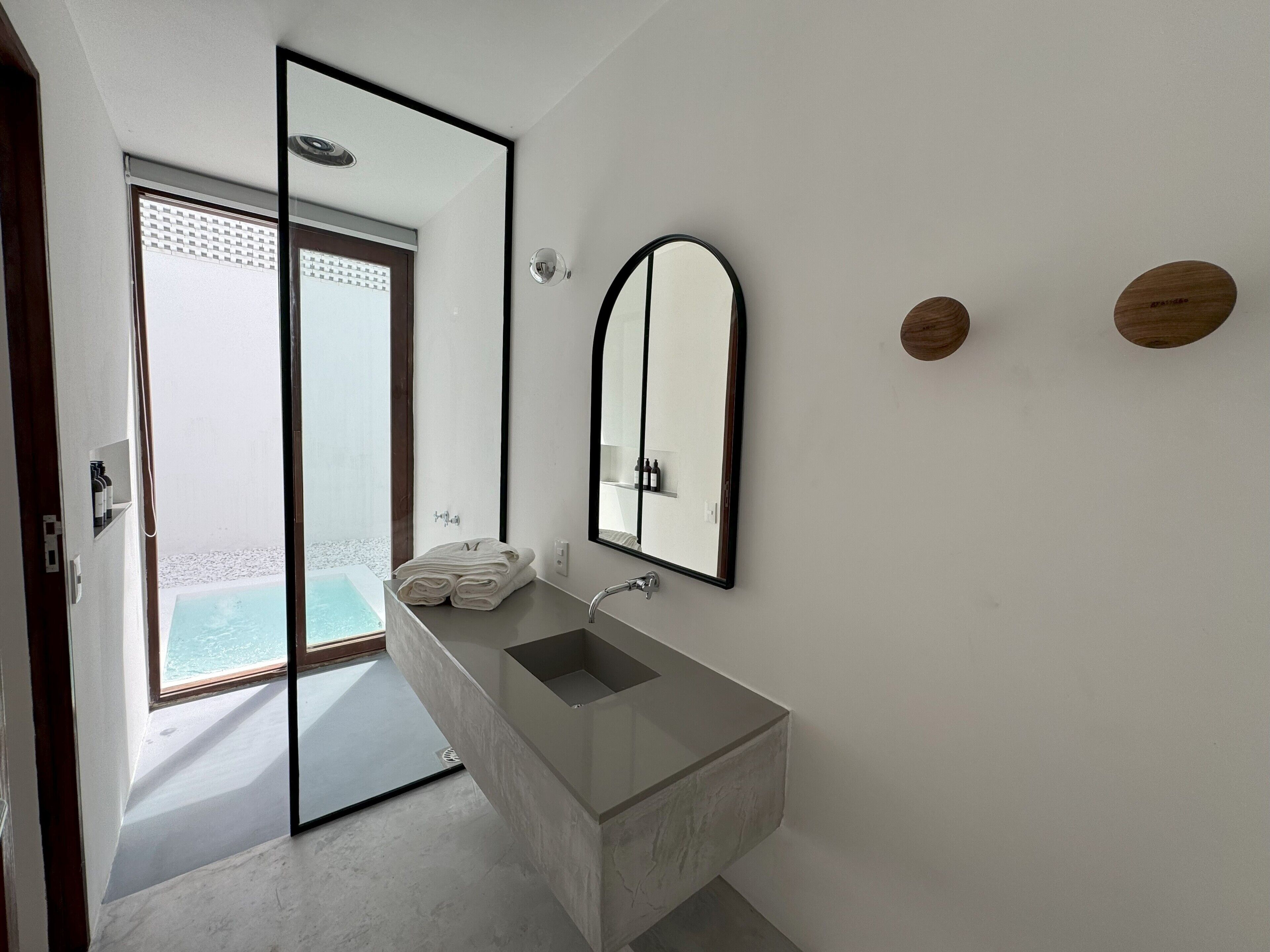 A modern bathroom with a large mirror, a sink, and a view of a pool.