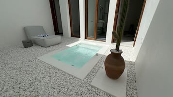 Uma área externa moderna com uma piscina retangular, pedras brancas, uma cadeira de descanso cinza e um cacto em vaso.