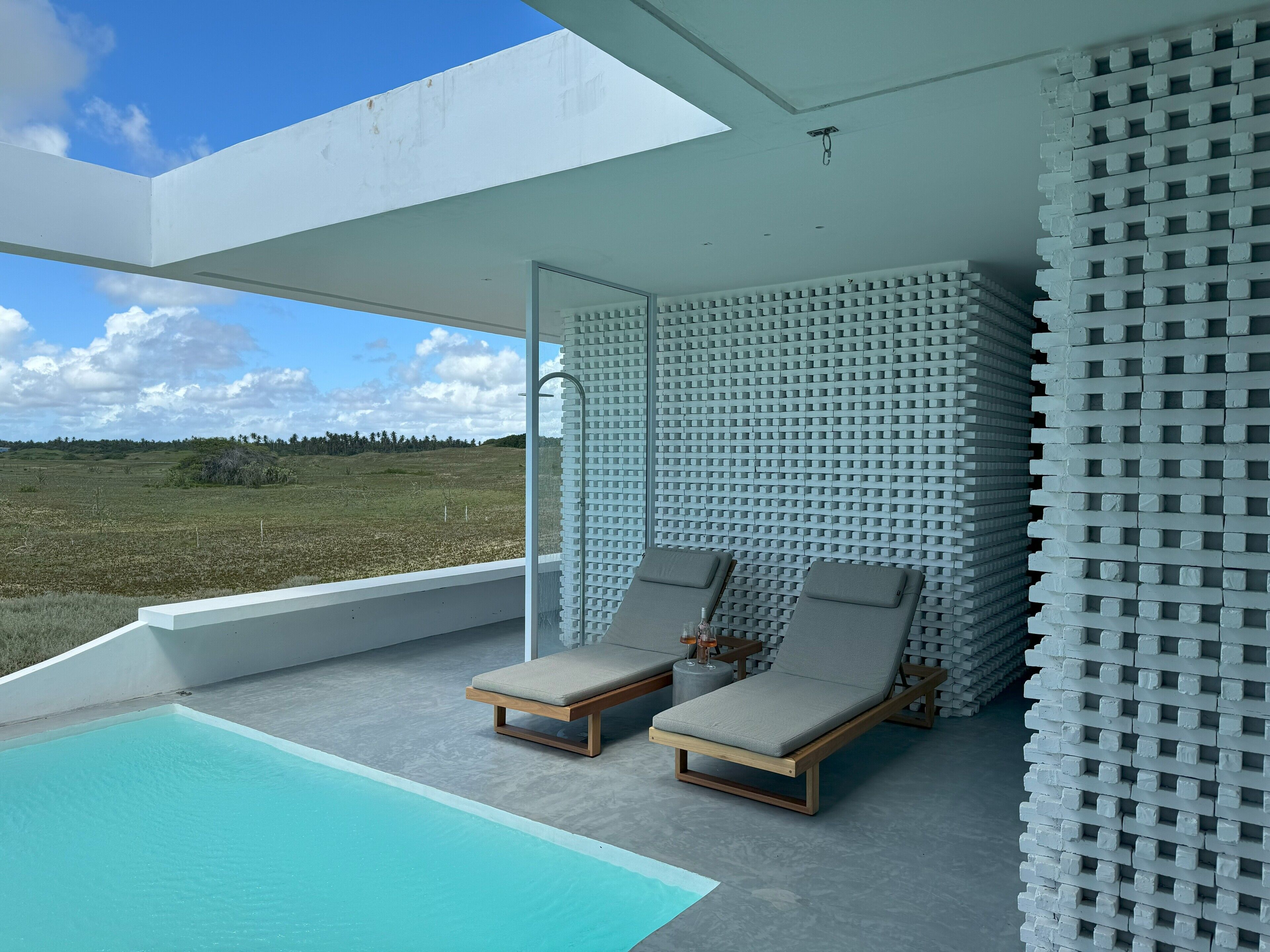 A modern outdoor pool area with two lounge chairs and a view of a natural landscape.