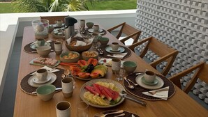 A dining table set with various dishes and drinks, overlooking a beach and ocean view.