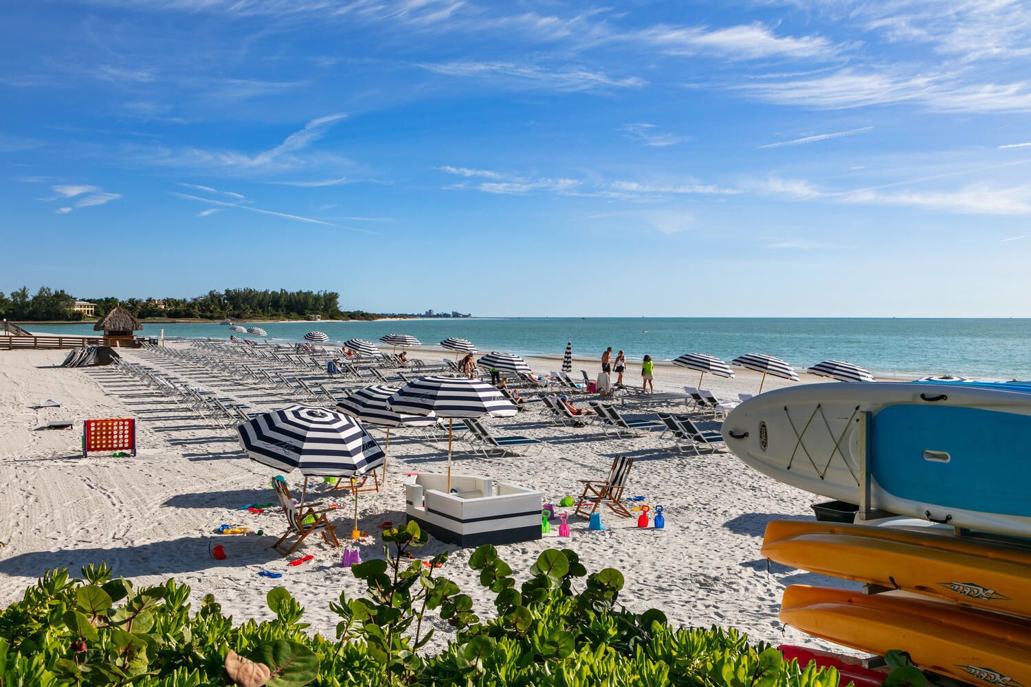 A beach with sun loungers and umbrellas, a lifeguard stand, and kayaks.