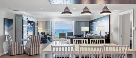 A modern hotel room with a dining area, a large window with a view of the ocean, and a ceiling with a skylight.