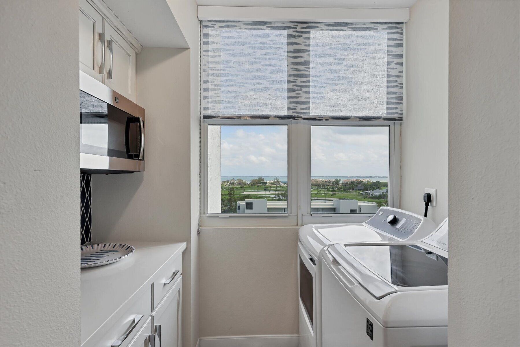 A laundry room with a large window, a washing machine, and a microwave.