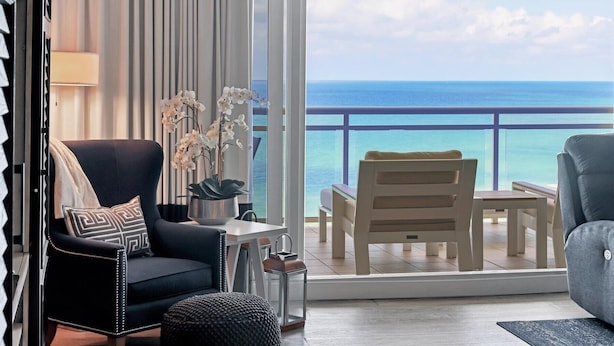 A balcony with a view of the ocean, a black sofa with patterned cushions, a wooden chair, and a small table with a lantern. - 2/2 Beachfront, VIEWS, Pool, Private Beach Access (Longboat Key)