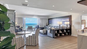 A spacious living area with a view of the ocean, a large sofa, a coffee table, striped armchairs, and a bookshelf with decorative items. - 2/2 Beachfront, VIEWS, Pool, Private Beach Access (Longboat Key)