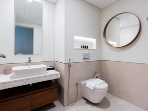Une salle de bain moderne avec un lavabo blanc, un meuble-lavabo en bois, des toilettes, une douche et un miroir rond accroché au mur.