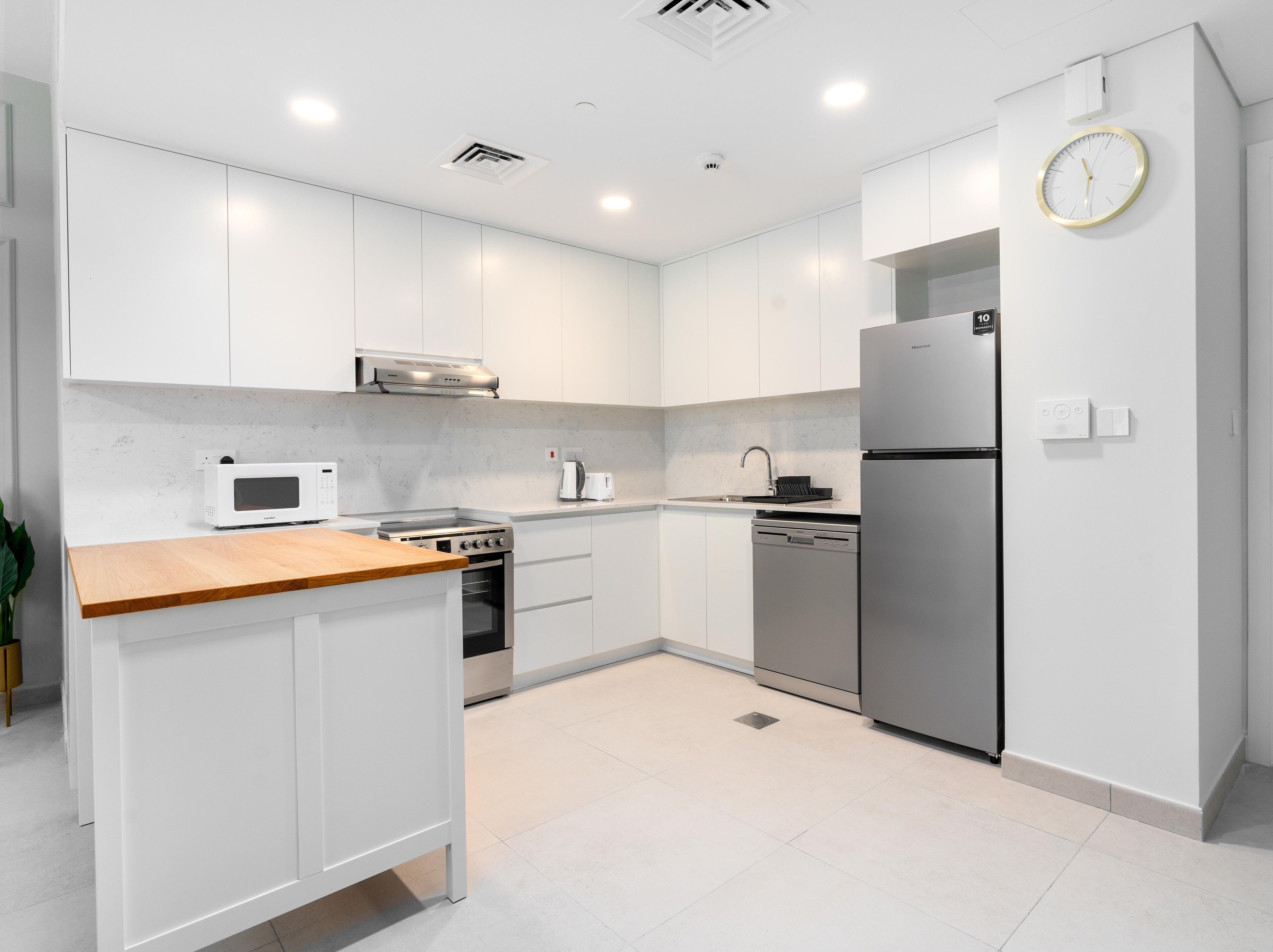 Une cuisine moderne avec des meubles blancs, un plan de travail en bois, des appareils électroménagers en acier inoxydable et une horloge murale.