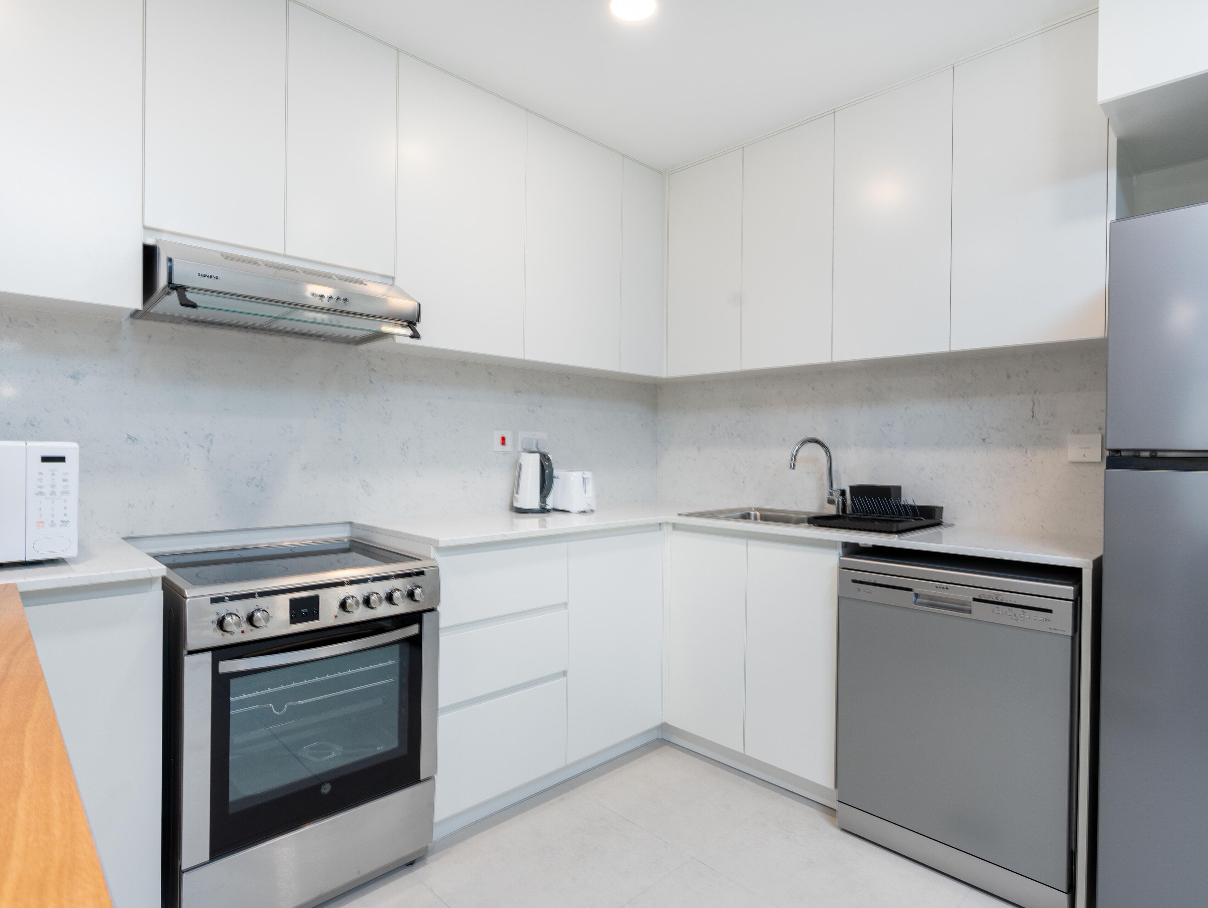 A modern kitchen with white cabinets, a built-in oven, a dishwasher, and a microwave.
