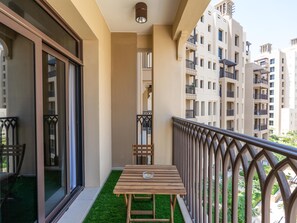 Un balcon avec une table et des chaises en bois, un petit coin de gazon artificiel et une vue sur les bâtiments voisins.