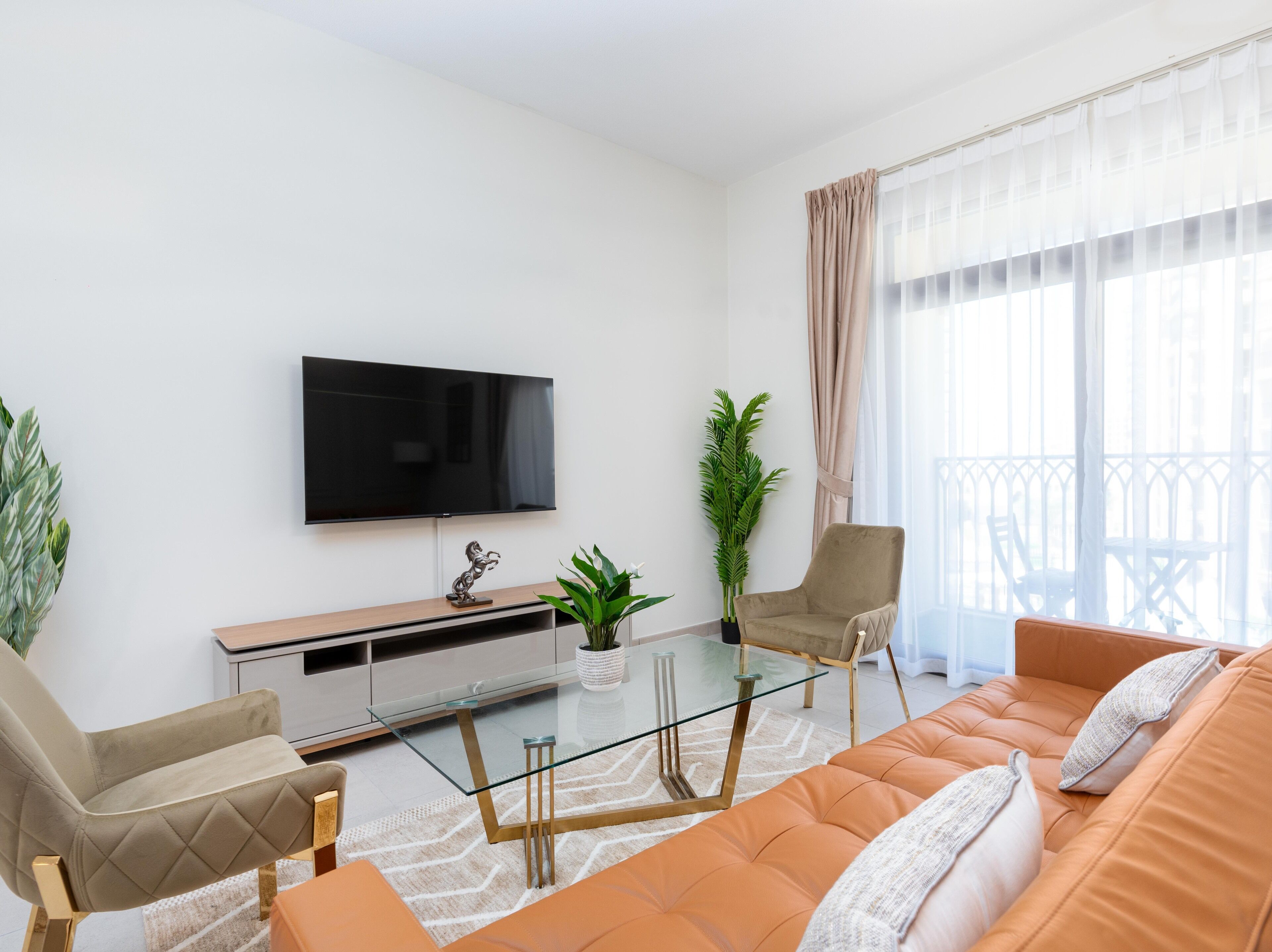 A modern living room with a flat-screen TV, a glass coffee table, a beige sofa, and a potted plant.