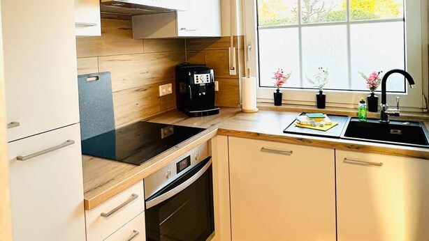 Cocina moderna con horno integrado, cafetera y ventana con vista a árboles.