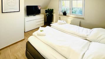 A bedroom with two beds, a TV, a dresser, a radiator, and a window.