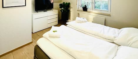 Une chambre avec deux lits, une télévision, une commode, un radiateur et une fenêtre.